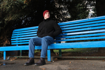 Man sitting on blue park bench looking pensive