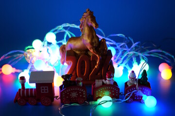 A horse figure with the number 2026 and a glowing Christmas tree garland. There is a toy train nearby.