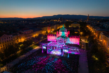 Aerial view of the Art Pavilion gleams with vibrant hues amidst the lively crowd, a beacon of culture against the twilight sky, Zagreb, Croatia.