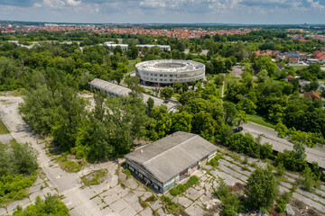 Aerial view of a unique circular building rising amidst a sea of lush greenery, contrasting sharply with the aging structures below, Zagreb, Croatia.