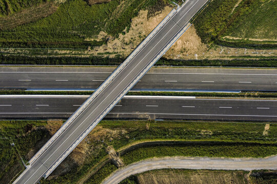 Aerial view of a highway intersected by a bridge, cutting through a landscape of green fields and earthy tones, Zagreb, Croatia.