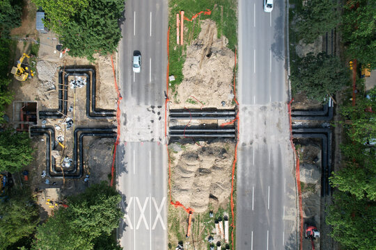 Aerial view of a road being constructed with pipes being laid, showing a contrast between the grey asphalt and the green trees, Zagreb, Croatia.