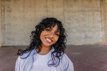 Smiling young woman with curly hair against concrete wall