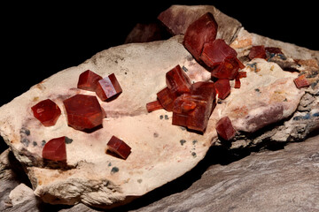 Striking photograph captures sharp red hexagonal Vanadinite crystals resting beautifully on a light colored natural rock matrix
