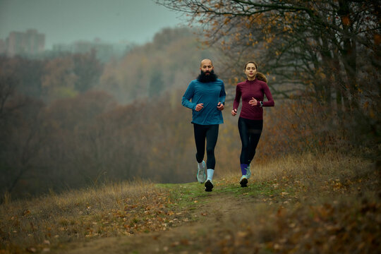Couple trail running forward on forest path with focused stamina. Concept of sports and fitness, fall marathon training, tourism adverts, lifestyle articles about staying active.