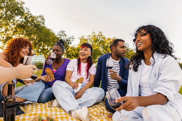 Diverse friends enjoying picnic in park drinking wine