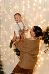 Mother holding baby boy playing with him and tossing him around in New Year's room