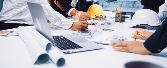 A diverse group of professionals engaged in collaborative planning over construction documents in a modern office setting. Tools and technology enhance productivity. SACTR