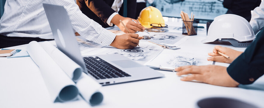 A diverse group of professionals engaged in collaborative planning over construction documents in a modern office setting. Tools and technology enhance productivity. SACTR