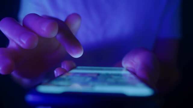 Close-up of hands holding a phone and scrolls social media feed at night. Concept of digital life, constant online interaction or technology overuse. 