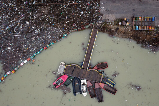 Aerial view of boats clustered near a wooden dock amidst murky waters, contrasting sharply with the adjacent polluted shoreline, Visegrad, Republika Srpska, Bosnia and Herzegovina.
