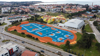 Aerial view of vibrant blue and orange sports courts contrasting with the surrounding green landscape and red-roofed buildings, Umag, Istria County, Croatia.
