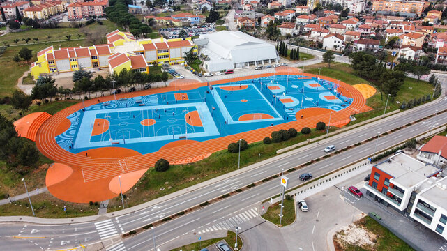 Aerial view of the vibrant blue and orange basketball courts contrasting with the surrounding buildings and roads, Umag, Istria County, Croatia.