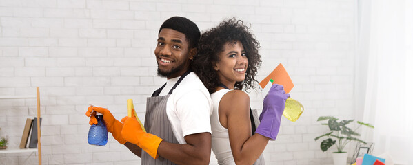 Smiling african american couple holding spray detergents, housekeeping and cleaning service concept