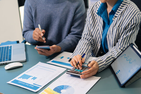 Business documents on office table with smart phone, tablet and laptop computer and graph with social network diagram and two colleagues discussing data in office.