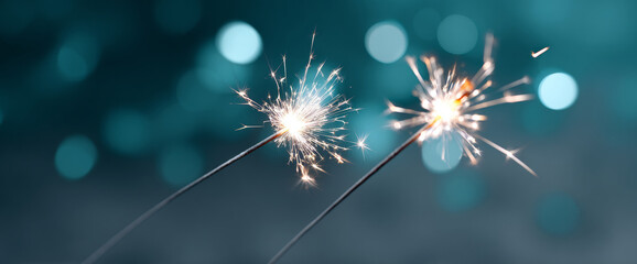 Close-up of two sparklers burning with bright sparks against a blurred blue bokeh background in a festive setting