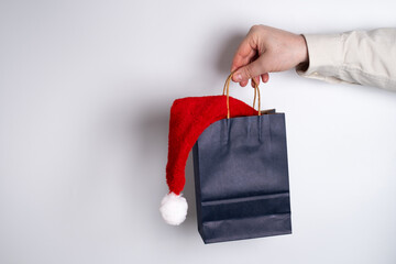 Hand holding paper shopping bag with santa hat inside