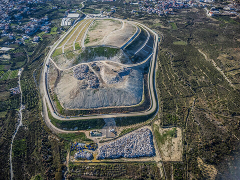 Aerial view of the stark contrast between the geometric landfill's grey slopes and the surrounding vibrant green landscape, Split, Split-Dalmatia County, Croatia.