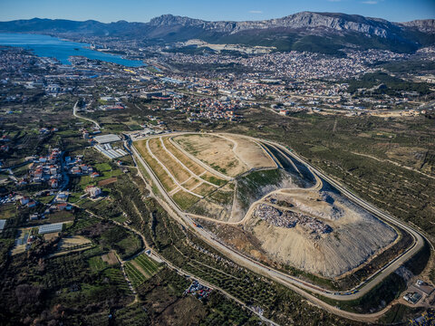 Aerial view of the vast landfill contrasting with the lush green landscape and distant mountains, showcasing environmental impact, Split, Split-Dalmatia County, Croatia.