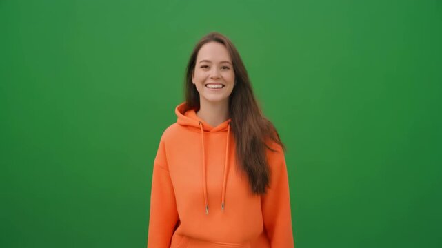 Smiling Young Woman in Orange Hoodie Pointing to the Side on Green Screen Background Keywords: woman, young, female, smiling, happy
