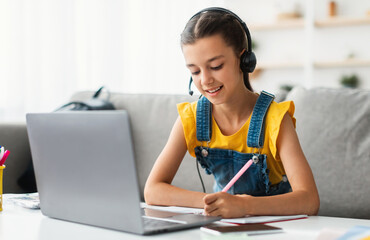 Homeschool little young girl student in headset learning during virtual internet online class with school teacher having remote meeting due to covid pandemic. Pupil studying foreign language or math