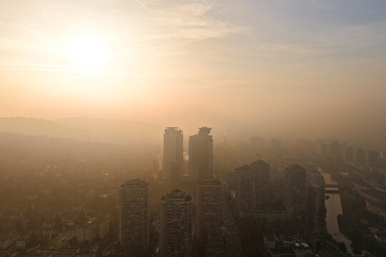 Aerial view of modern buildings piercing through a hazy cityscape at sunset, casting long shadows over the Miljacka River, Sarajevo, Federation of Bosnia and Herzegovina, Bosnia and Herzegovina.