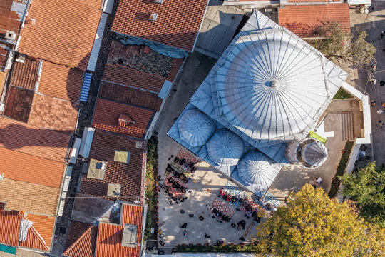 Sarajevo, Bosnia and Herzegovina - 17 November 2025: Aerial view of the Gazi Husrev-beg Mosque, its silver dome gleaming amidst a tapestry of red-tiled roofs and gathering crowds.