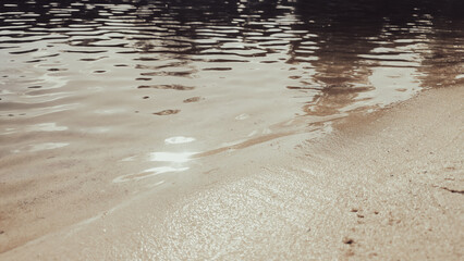Reflection of clouds and sky in calm lake water with a sandy shore.