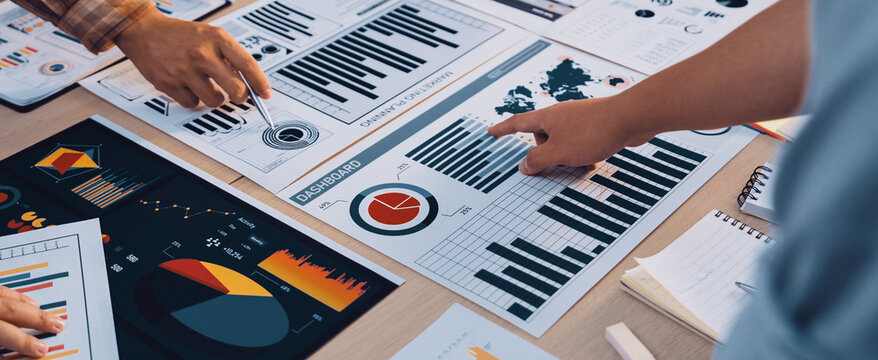 A diverse business team engages in data analysis during a meeting. They explore graphs and charts to make informed strategic decisions in a modern office setting. SACTR - Powered by Adobe