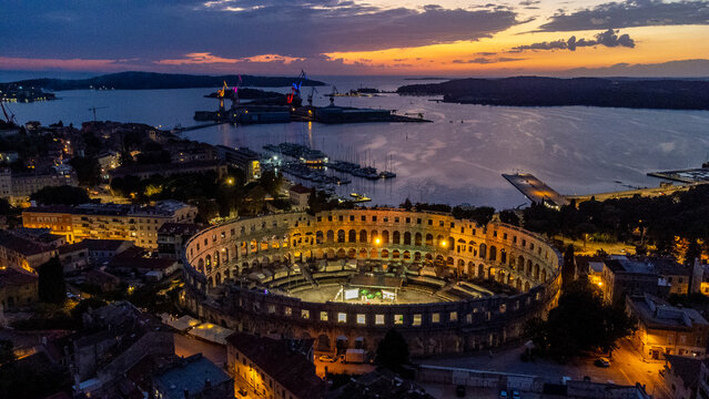 Aerial view of the illuminated Pula Arena standing proud against the fading twilight over the Adriatic Sea, a beacon of history and architectural wonder, Pula, Istria County, Croatia.