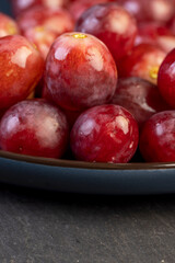 red ripe grapes in drops of water on a blue plate , wet ripe and delicious red grapes on a plate on a black slate board