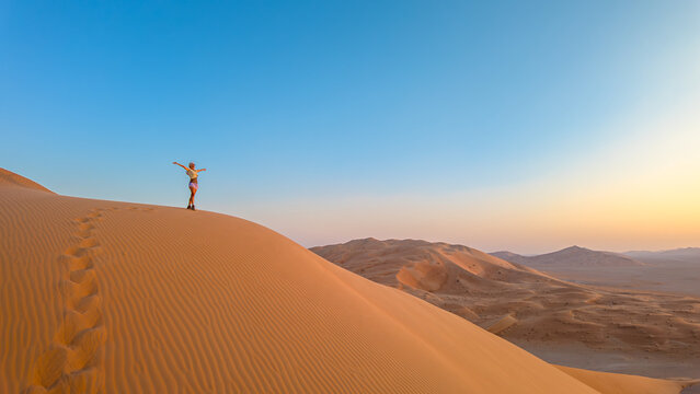 Aerial view of an adventure woman conquering Empty Quarter dunes in Oman, a solitary ascent against golden sands. Girl climbing the Rub' al-Khali desert dunes at sunset.