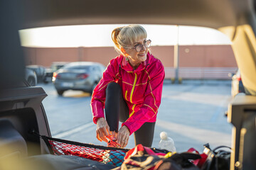 Mature woman tying shoelaces on a car trunk before jogging
