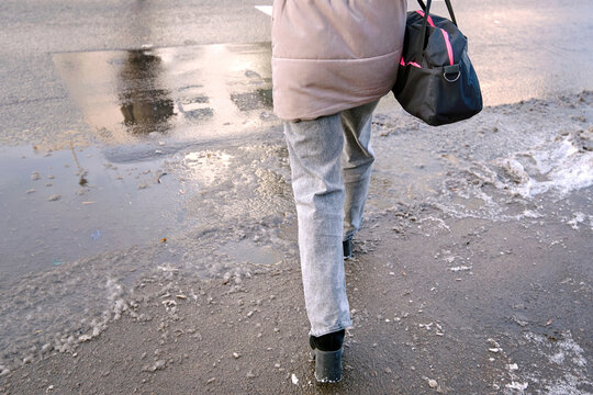 Pedestrian woman walking over melting slush at road crossing on wet winter day, struggle to avoid slushy puddles and the potential slipping danger in icy urban conditions