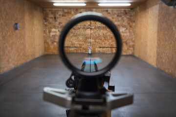 First person view looking through a rifle optical sight aiming at a metal popper target at an indoor shooting range