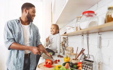 Cute little african american girl and her dad cooking in kitchen at home