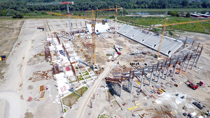 Aerial view of a stadium under construction with cranes overseeing the skeletal structure against a backdrop of a wide river, Osijek, Osijek-Baranja County, Croatia.