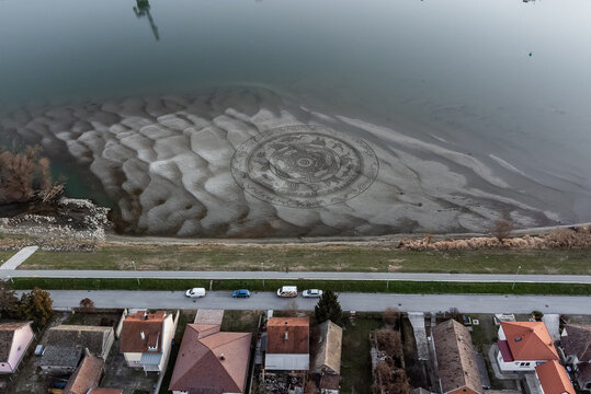 Aerial view of a captivating sand art mandala, etched into the banks of the Drava River near houses under a gray sky, Osijek, Osijek-Baranja County, Croatia.