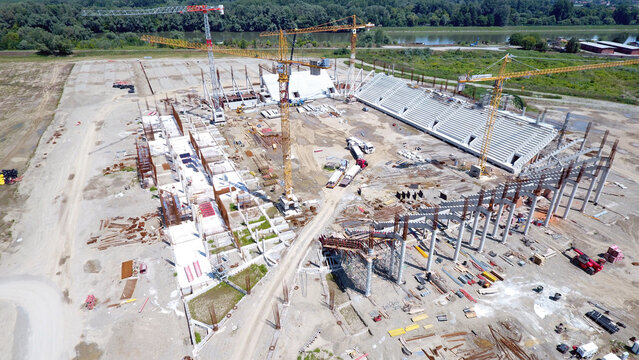 Aerial view of a stadium under construction with cranes overseeing the skeletal structure against a backdrop of a wide river, Osijek, Osijek-Baranja County, Croatia.