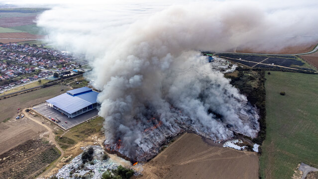 Aerial view of a thick plume of smoke billowing from a burning landfill near a building, casting a stark contrast against the muted landscape, Osijek, Osijek-Baranja County, Croatia.
