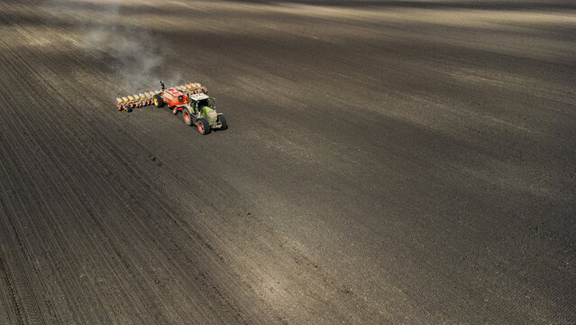 Aerial view of a tractor tilling the dark soil, creating linear patterns across the expansive field, Osijek, Osijek-Baranja County, Croatia.