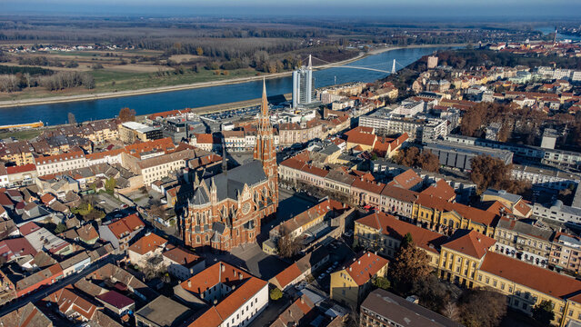Aerial view of the striking red-brick architecture of St. Peter and Paul Church contrasts against the serene Drava River and distant bridge, Osijek, Osijek-Baranja County, Croatia.