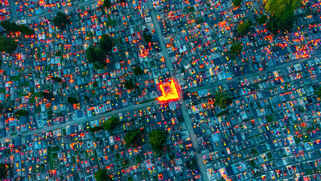 Aerial view of countless candles flicker atop graves in a vast cemetery, casting an ethereal orange glow against the cool twilight, Osijek, Osijek-Baranja County, Croatia.