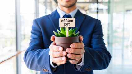 Employee in office holding potted plant with label 'office pet', sunlight through windows, workplace relaxation, greenery, enhancing office decor, suitable for business blogs or wellness articles