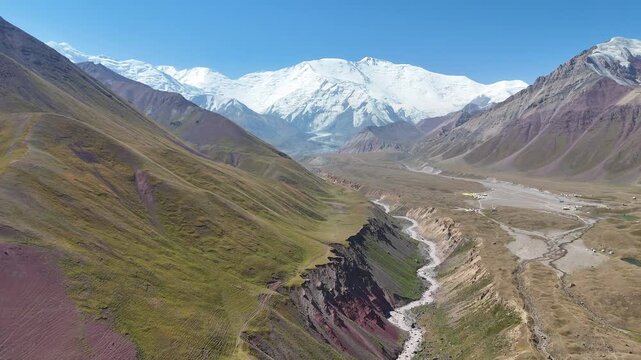 This aerial video reveals the breathtaking scenery of the Alay Valley in Kyrgyzstan, where the majestic Lenin Peak rises above the Chon-Alay mountain range under a perfectly clear sky.