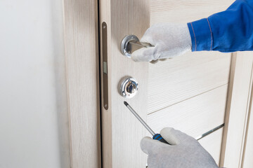 the master's hands install the door lock of the interior door using a screwdriver, close-up