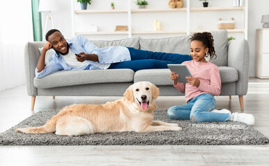 Portrait of happy African American family spending time together, daughter sitting on the floor...