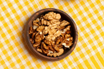 Overhead shot of shelled walnuts in a small round wooden bowl on checkered fabric
