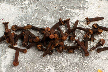 Dried brown whole cloves spice scattered horizontally on a rustic gray textured background