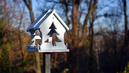 Wooden bird feeder with berries and wheat inside, birdhouse on a beautiful blurred background of yellow leaves outdoors. feeders in the autumn park. feed wild birds during the cold season